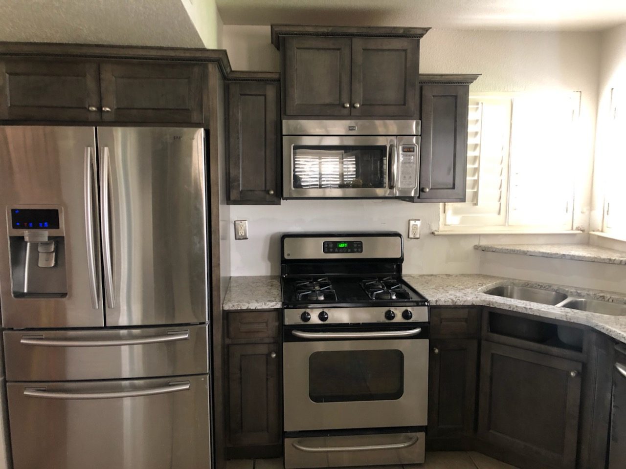 Dark-stained kitchen cabinets around the refrigerator and microwave with granite counters