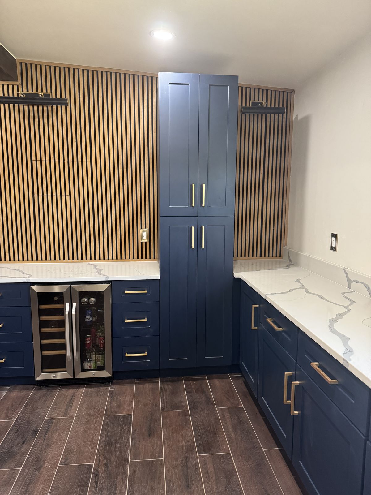 Navy blue bar cabinets with gold pulls, tall pantry, wine fridge and a wood slat accent wall