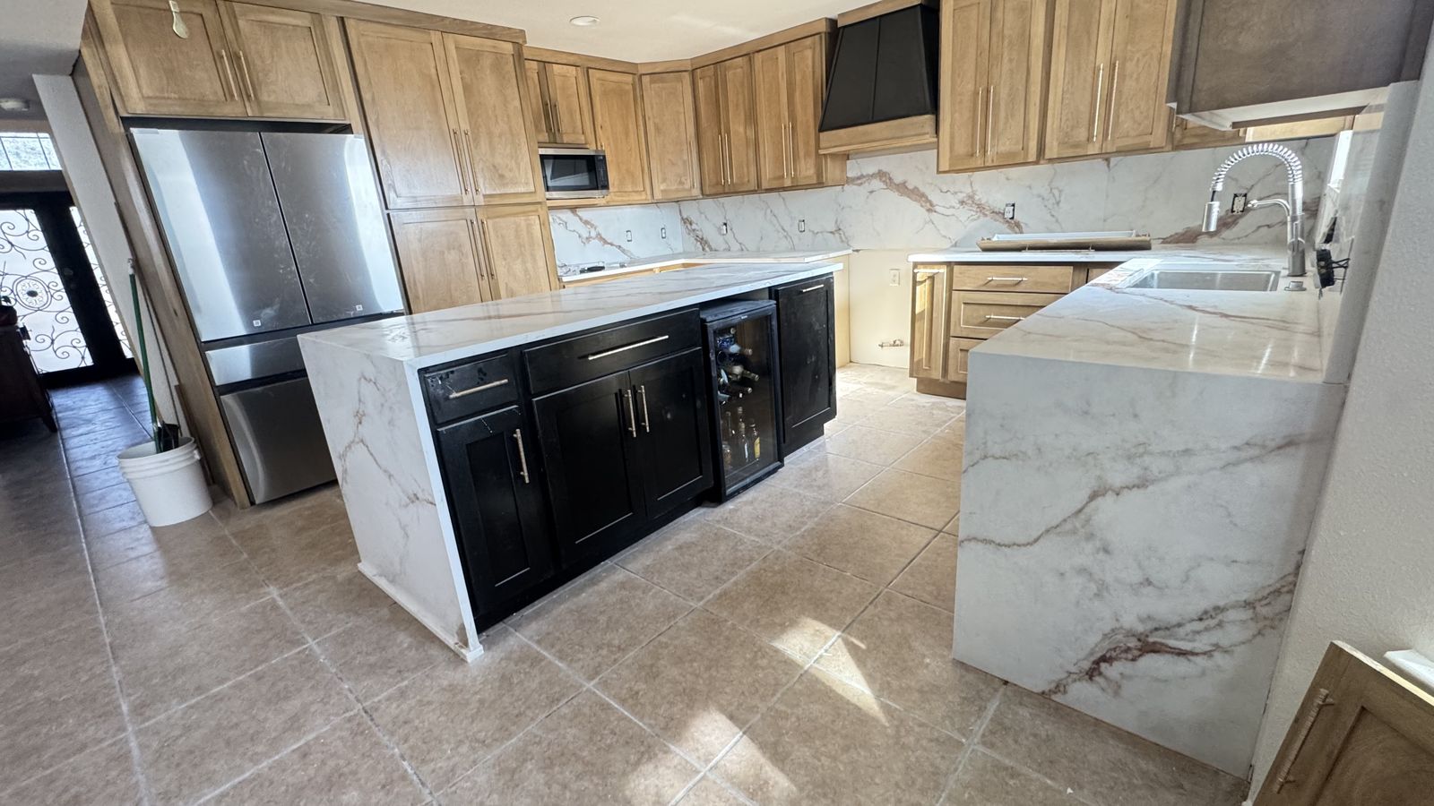 Kitchen with black island cabinets under a marble waterfall countertop and built-in wine fridge