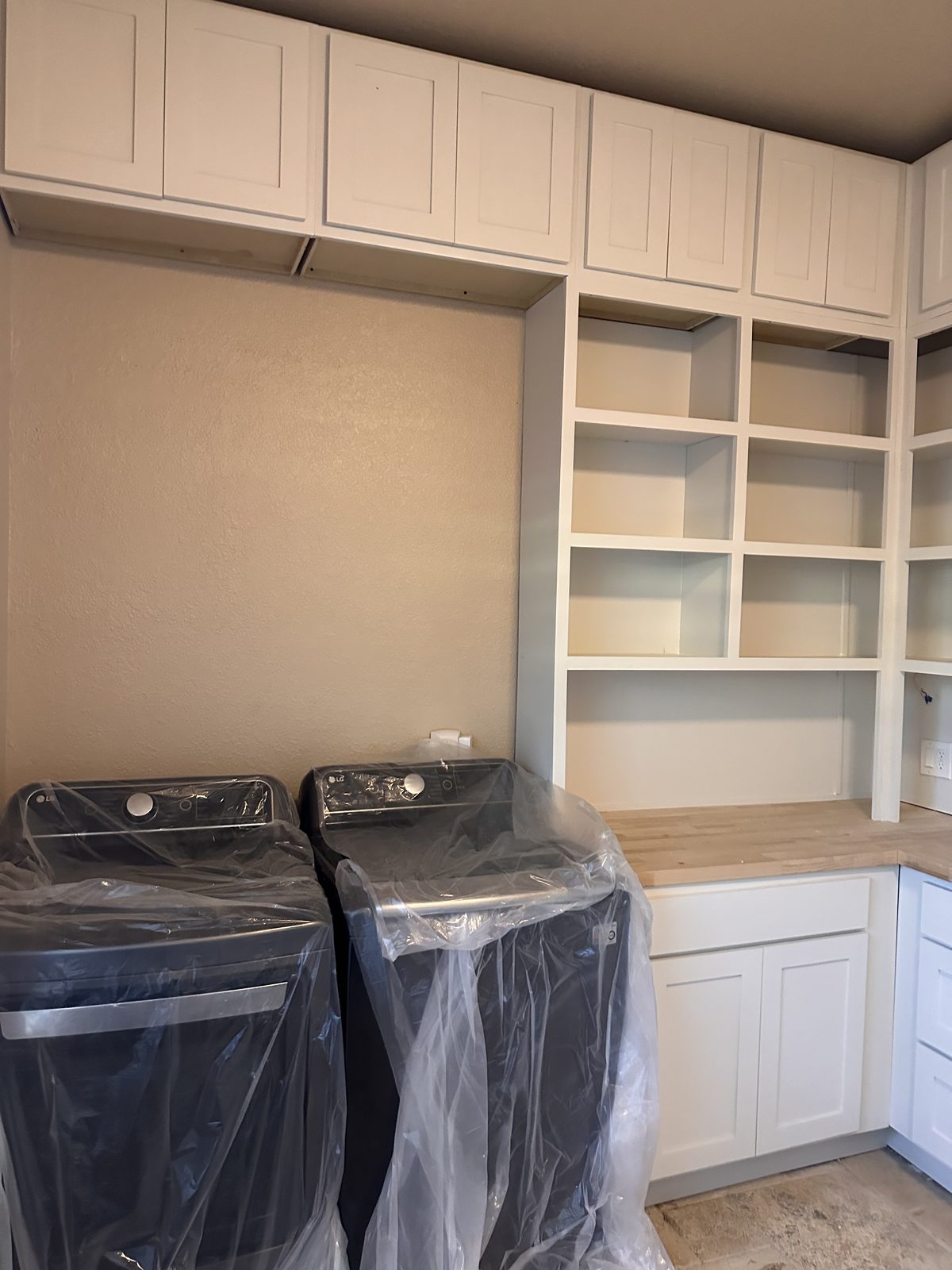 Laundry wall with white shaker upper cabinets, open cubby shelving and a butcher-block counter next to the washer and dryer